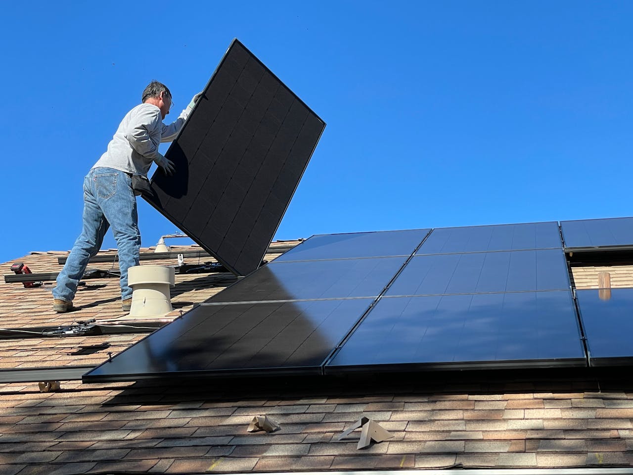 about-us-01 A worker installs solar panels on a sunny day, highlighting renewable energy solutions.
